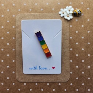 May include: A rainbow enamel pin on a white card with the text "with love..." and a small red heart.