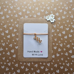 May include: A white card with a brown border on a brown background with a white heart pattern. The card has a string with a gold candy charm and the text "Hand Made With Love".
