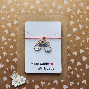 May include: A white card with a red string and a rainbow charm with a happy face. The card says "Hand Made with Love" and has a pink heart.