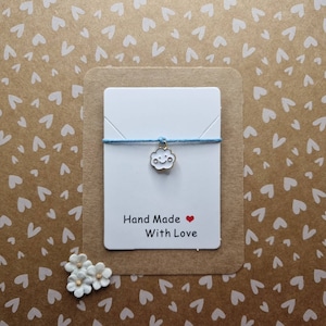May include: A white card with blue string and a gold charm shaped like a smiling cloud. The card says "Hand Made with Love" and has a red heart.