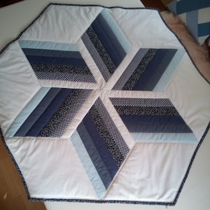 Könnte beinhalten: Ein weißer sechseckiger Tischläufer mit einem blauen und hellblauen Sternmuster. Der Stern besteht aus Stoffstreifen, die in einem geometrischen Muster zusammengenäht sind.