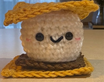 Könnte beinhalten: Ein gehäkeltes Plüschtier in Form eines Marshmallow-Brötchens. Das Marshmallow ist weiß mit schwarzen Augen und einem schwarzen Lächeln. Die Graham-Cracker sind gelb.