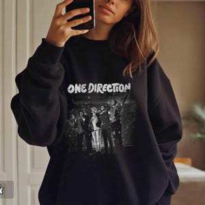 May include: Black sweatshirt featuring the text "ONE DIRECTION" in white, above a black and white image of the band. The sweatshirt is a crew neck style.