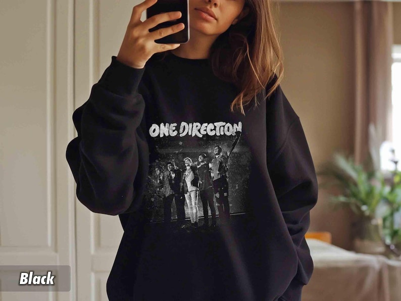 May include: Black sweatshirt featuring the text "ONE DIRECTION" in white, above a black and white image of the band. The sweatshirt is a crew neck style.