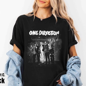 May include: Black t-shirt with the text "ONE DIRECTION" in white, above a grayscale image of the band. The shirt also has the text "Comfort C. Black" in the bottom left corner.