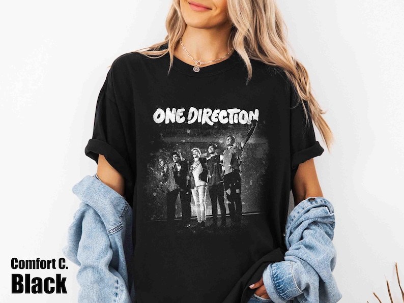 May include: Black t-shirt with the text "ONE DIRECTION" in white, above a grayscale image of the band. The shirt also has the text "Comfort C. Black" in the bottom left corner.
