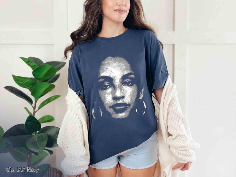 Peut inclure: Un t-shirt bleu marine avec un motif blanc repr&eacute;sentant le visage d'une femme. Le motif est un gros plan du visage de la femme, et il comprend ses yeux, son nez, sa bouche et ses boucles d'oreilles.