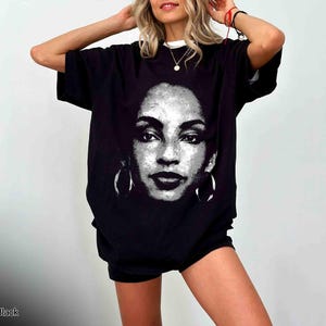 Peut inclure: T-shirt noir avec un imprim&eacute; graphique d'un visage de femme. Le visage est en noir et blanc et porte de grandes boucles d'oreilles.