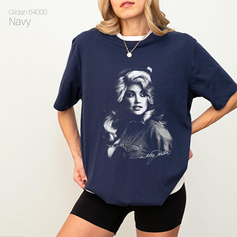 May include: Navy blue t-shirt featuring a black and white portrait of a celebrity with signature. The shirt has a white collar and the text "Gildan 64000 Navy" is printed on the upper left side.