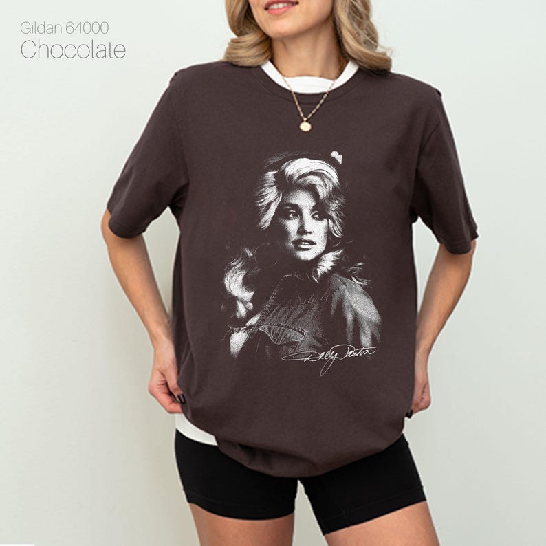 May include: Chocolate-colored t-shirt with a white collar featuring a black and white portrait of a woman. The text "Dolly Parton" is printed below the portrait. The shirt is a Gildan 64000.