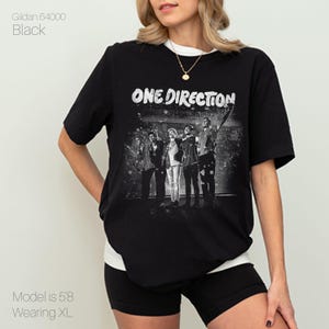May include: Black t-shirt with a black and white graphic of the band One Direction and the band's name in white. The shirt is a Gildan 64000, size XL. The model is 5'8.