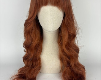 May include: A long, wavy, auburn-colored wig with bangs. The wig is styled in loose waves and has a natural-looking parting.