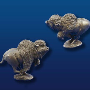 May include: Two silver-colored metal figurines of a bison running. The bison are in a dynamic pose with their legs outstretched and their heads turned to the side. The figurines are set against a blue background.