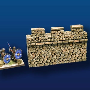 May include: Two miniature figures of soldiers with shields and spears stand in front of a stone wall with a rough texture. The wall is made of small, irregular stones and has a brown color.