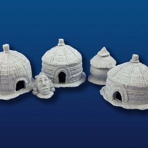 Op de afbeelding: Vier miniatuur rieten hutten, waarvan één met een gesneden houten gezicht, gemaakt van wit hars.