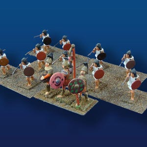 May include: Miniature figurines of ancient warriors, each holding a spear and shield. The figures are dressed in white tunics and helmets, with shields in shades of brown, red, and green. They stand on a textured, tan base against a blue background.