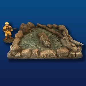 May include: A miniature model of a beaver trapped in a rocky stream with a small figure of a person holding a rifle standing nearby.