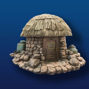May include: A miniature stone cottage with a thatched roof. The cottage features a wooden door and is surrounded by rocks. Two teal-colored containers are placed on either side of the cottage.