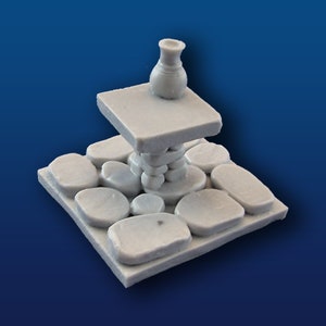 May include: A miniature stone platform with a small ceramic vase on top. The platform is made of stacked stones and has a square base.