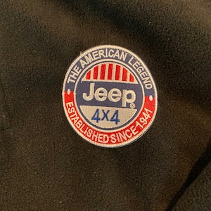 May include: Circular patch with the text "THE AMERICAN LEGEND" and "ESTABLISHED SINCE 1941". The patch features the Jeep logo in blue and red, with "4X4" below. The patch is on a black background.