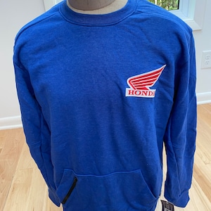 May include: Royal blue sweatshirt with a kangaroo pocket and a black zipper. The Honda logo, featuring a red wing and the brand name, is on the upper left chest. The sweatshirt is displayed on a mannequin.
