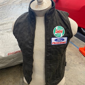 May include: A dark gray quilted vest with a full-length zipper. The vest features a Castrol Motor Oil patch and a Ford Racing patch. The vest is displayed on a mannequin.
