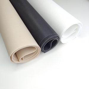 K&ouml;nnte beinhalten: Drei Rollen Stoff in Beige, Schwarz und Wei&szlig;. Der Stoff ist aufgerollt und die Enden sind sichtbar.