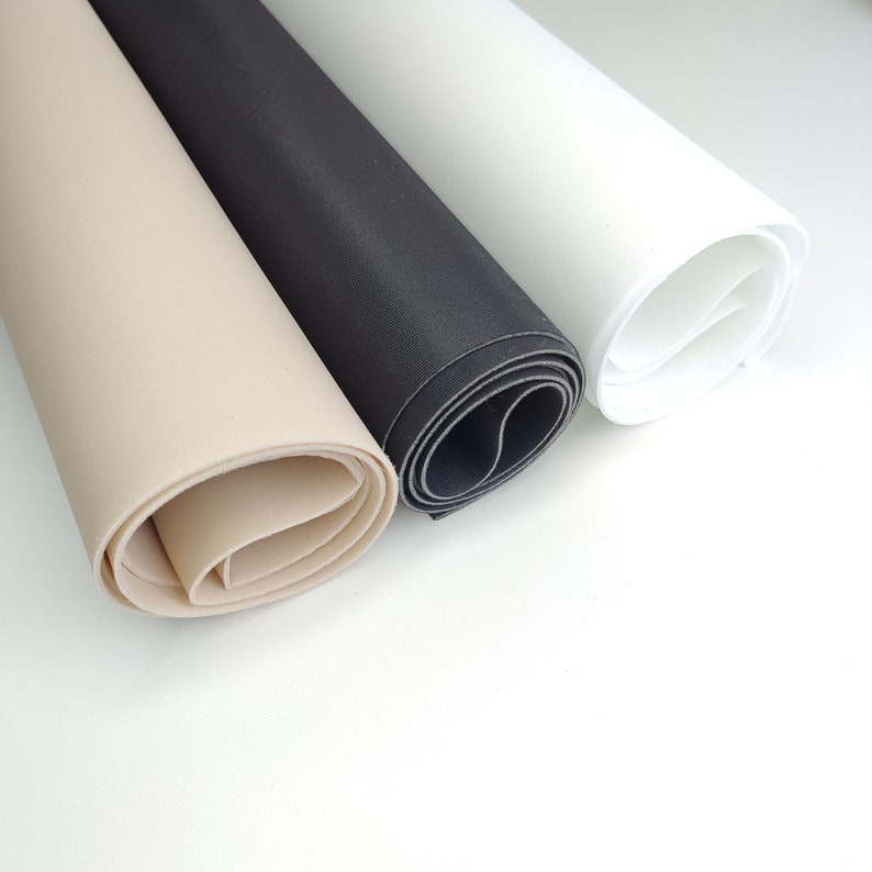 K&ouml;nnte beinhalten: Drei Rollen Stoff in Beige, Schwarz und Wei&szlig;. Der Stoff ist aufgerollt und die Enden sind sichtbar.