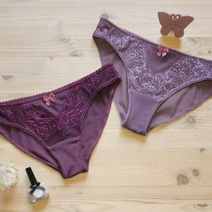 May include: Two pairs of purple lace underwear with a bow detail. The underwear is on a light wood surface.