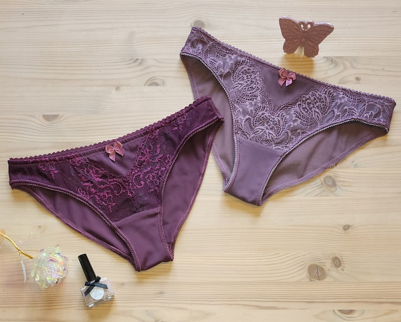 May include: Two pairs of purple lace underwear with a bow detail. The underwear is on a light wood surface.