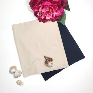 May include: Two fabric swatches, one beige and one navy blue, are folded together on a white surface. A seashell is placed on top of the beige fabric.
