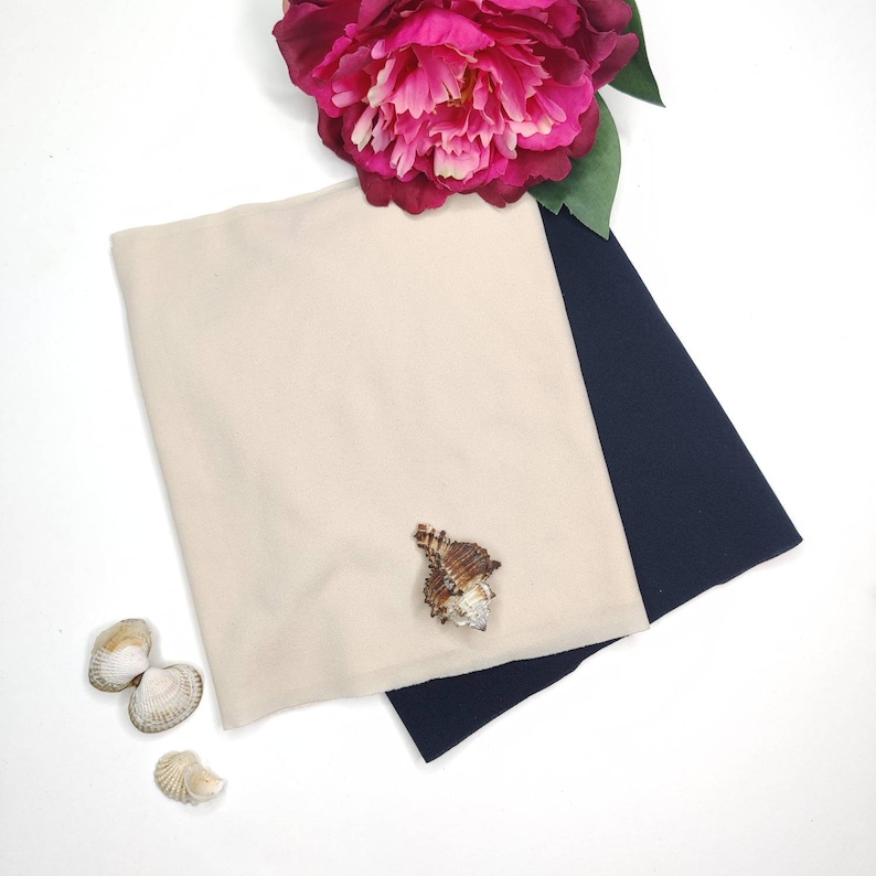 May include: Two fabric swatches, one beige and one navy blue, are folded together on a white surface. A seashell is placed on top of the beige fabric.