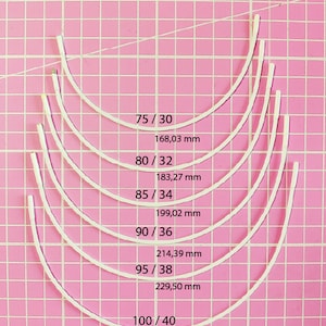 Può includere: Un set di sei coppe per reggiseno con ferretto bianco in diverse misure, misurate in pollici e millimetri, su uno sfondo a griglia rosa.
