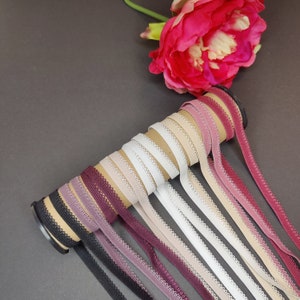 May include: A roll of 10 different colors of elastic trim with scalloped edges. The trim is arranged in a rainbow pattern, with the darkest colors at the bottom and the lightest colors at the top.