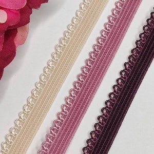 May include: Three different colors of elastic trim with a scalloped edge. The colors are beige, pink, and burgundy.