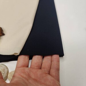 May include: A close-up of a dark blue fabric swatch. The fabric is smooth and has a slight sheen. The swatch is folded in half and is being held by a hand.