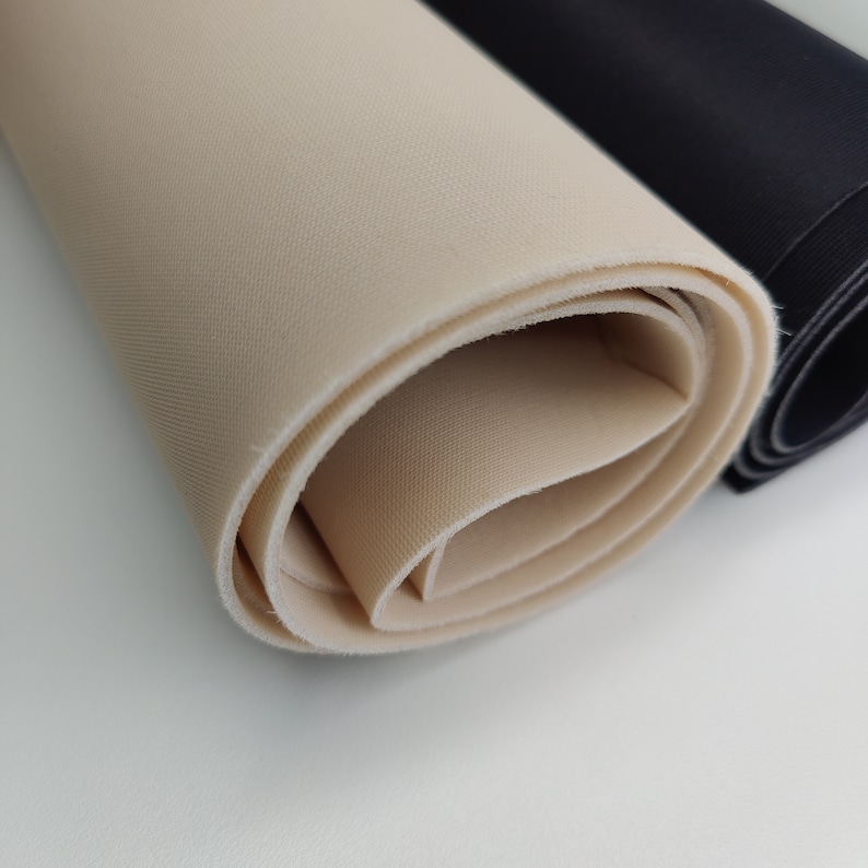 K&ouml;nnte beinhalten: Zwei Stoffrollen, eine beige und eine schwarze, sind aufgerollt und nebeneinander gelegt. Die beige Stoffrolle liegt auf der schwarzen Stoffrolle.