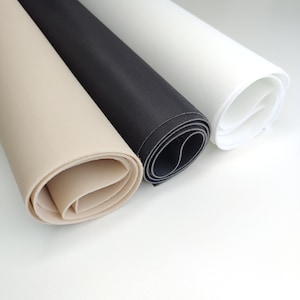 Puede incluir: Tres rollos de tela en diferentes colores: beige, negro y blanco. La tela está enrollada y los bordes son visibles.