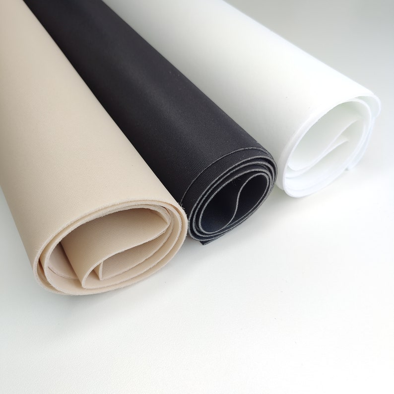 K&ouml;nnte beinhalten: Drei Rollen Stoff in verschiedenen Farben: beige, schwarz und wei&szlig;. Der Stoff ist aufgerollt und die Kanten sind sichtbar.
