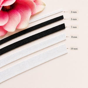Könnte beinhalten: Nahaufnahme von Gummibändern in verschiedenen Breiten: 3 mm, 5 mm, 7 mm, 8 mm und 10 mm. Die Bänder sind schwarz und weiß und parallel angeordnet. Eine rosa Blume befindet sich in der oberen linken Ecke.