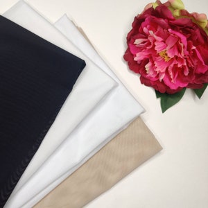 Könnte beinhalten: Ein Stapel Stoffmuster in Schwarz, Weiß und Beige. Der Stoff ist glatt und scheint ein leichtes Material zu sein.