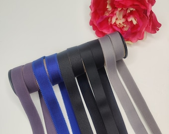 Könnte beinhalten: Eine Sammlung von sieben elastischen Bändern in verschiedenen Farben, darunter Grau, Schwarz, Blau und Lila. Die Bänder sind aufgerollt und in einer Reihe angeordnet.
