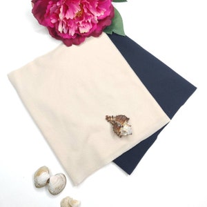 May include: A beige and navy blue fabric swatch with a seashell on top. The fabric is soft and smooth, and the seashell is a natural, light brown color.