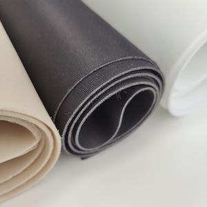 K&ouml;nnte beinhalten: Drei Rollen Stoff in verschiedenen Farben: beige, schwarz und wei&szlig;. Der Stoff ist aufgerollt und die Kanten sind sichtbar.