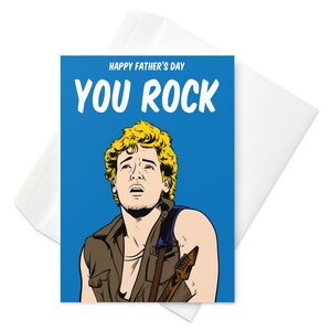 May include: A greeting card with a blue background and a cartoon illustration of a man with blonde hair holding a guitar. The text "HAPPY FATHER'S DAY YOU ROCK" is printed in white on the card.