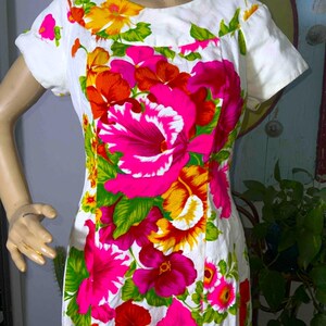 May include: White dress with a vibrant floral print featuring large pink, red, yellow, and orange flowers. The dress has short sleeves and a scoop neckline. The floral pattern is set against a white background.