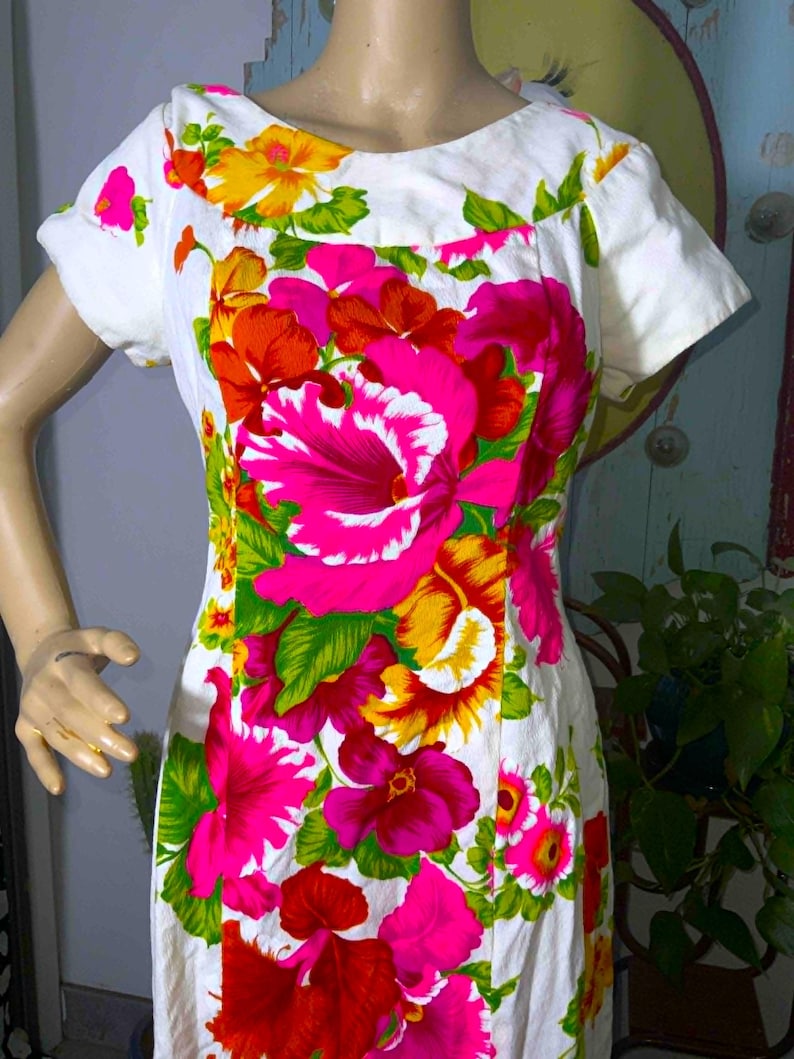 May include: White dress with a vibrant floral print featuring large pink, red, yellow, and orange flowers. The dress has short sleeves and a scoop neckline. The floral pattern is set against a white background.