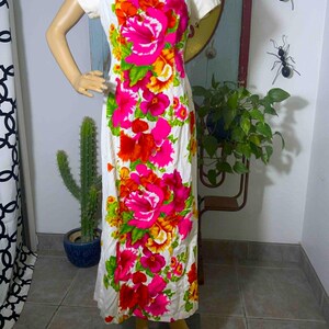 May include: A white, short-sleeved dress with a vibrant floral pattern in shades of pink, red, orange, and yellow. The flowers are large and prominent against the white background. The dress has a simple, classic silhouette.