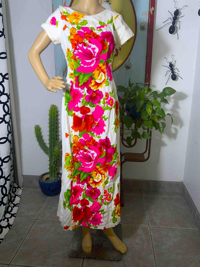 May include: A white, short-sleeved dress with a vibrant floral pattern in shades of pink, red, orange, and yellow. The flowers are large and prominent against the white background. The dress has a simple, classic silhouette.
