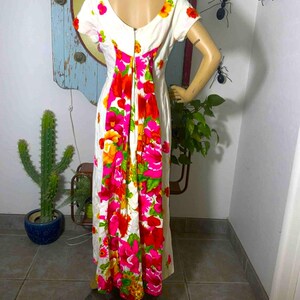 May include: A vintage white maxi dress with a scoop back and short sleeves. The dress features a vibrant floral pattern in shades of pink, red, orange, and yellow. The flowers cascade down the back of the dress, creating a bold and eye-catching design.